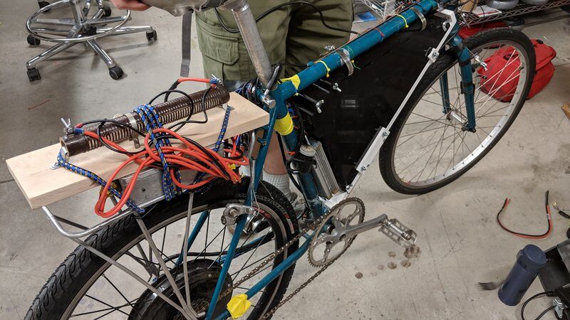Bicycle mid-conversion in a workshop, with motor wiring and a mounted battery enclosure