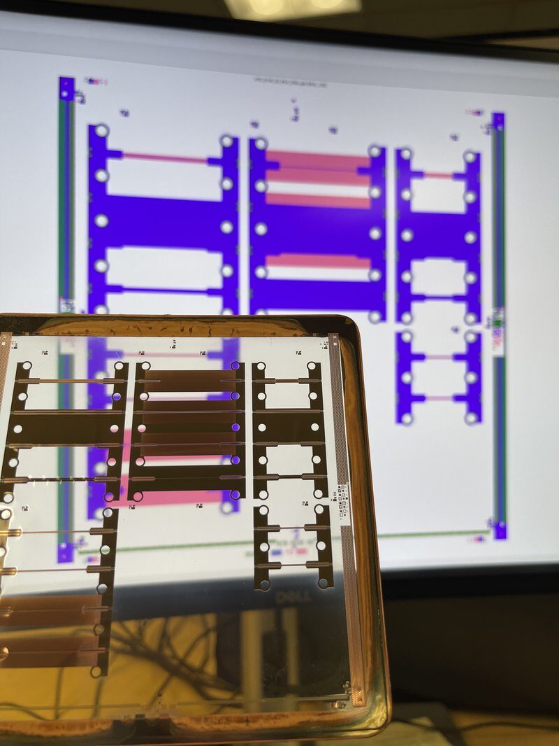 Flexible PCB panel held in front of a monitor showing its CAD layout