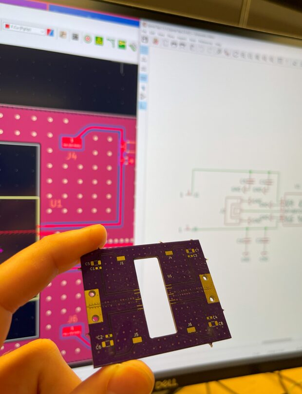 Bare amplifier PCB held in front of its KiCad layout