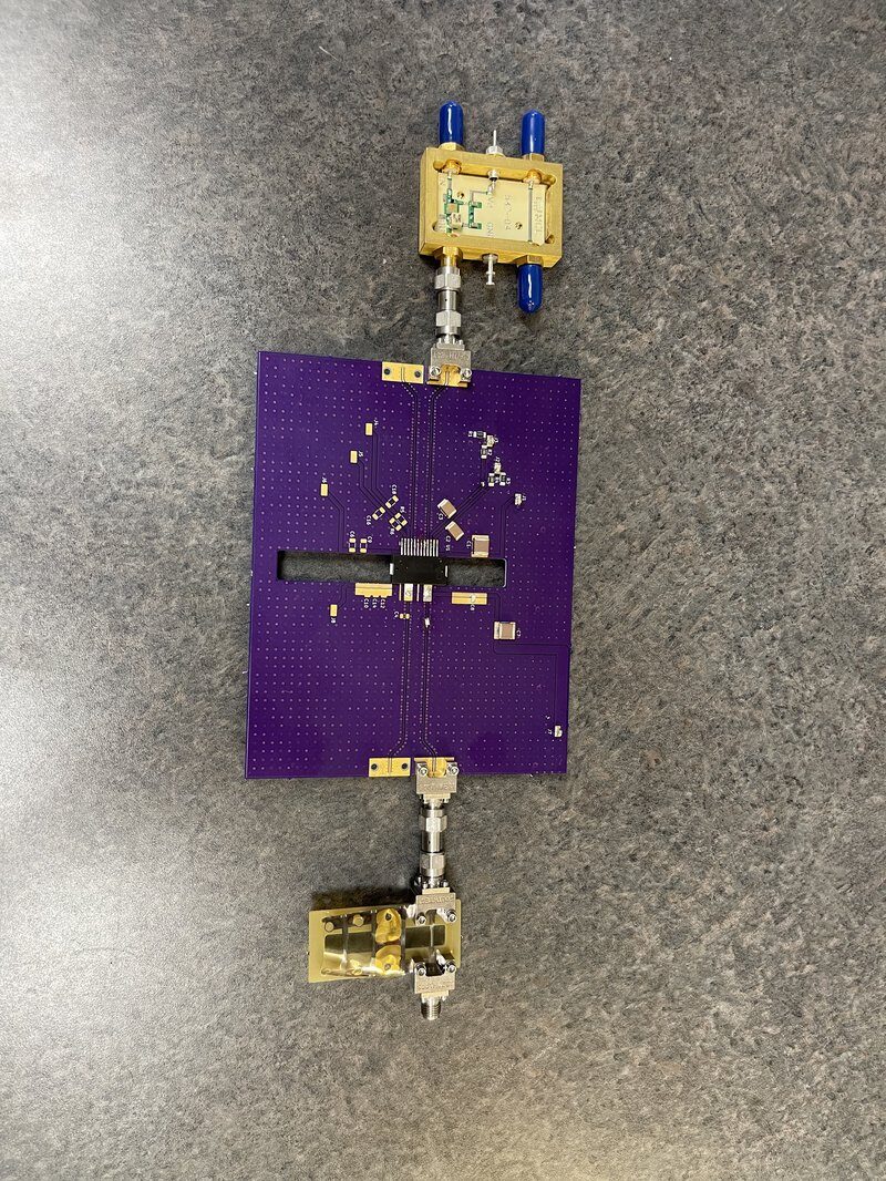 Purple RF amplifier PCB connected to gold-plated test fixtures on a lab bench